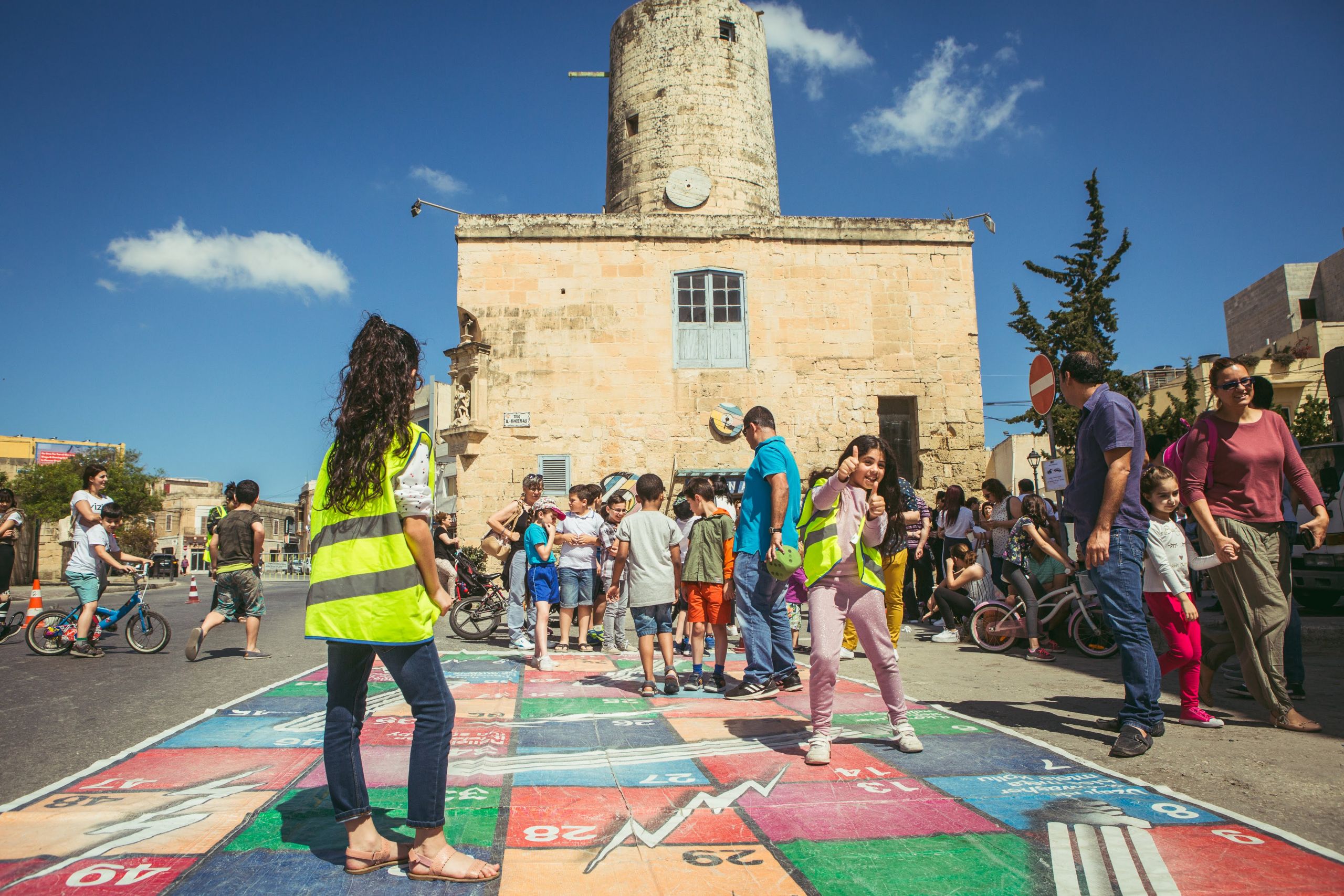 Photo showing The Mill in the background and children and adults in the foreground playing during a morning activity